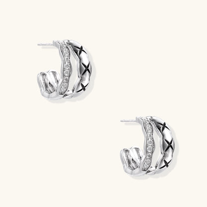 Close-up of gold-plated huggie earrings featuring X-pattern band and wavy zirconia-set band on white background.