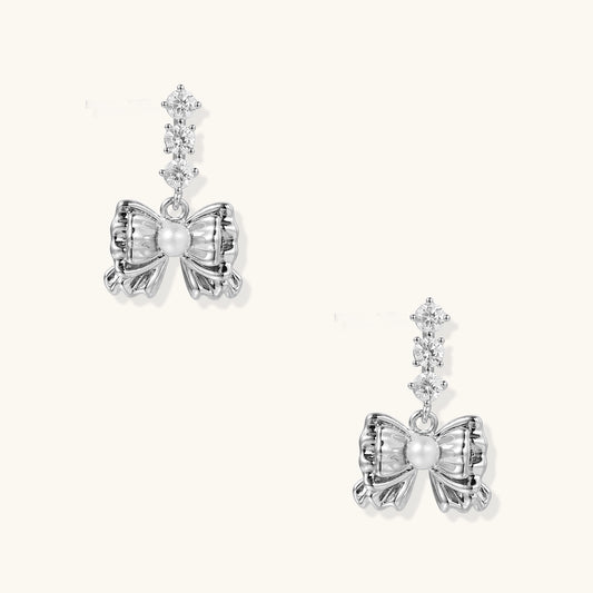 Delicate gold-plated bow drop earrings with three zirconia crystals and center pearl on white background.