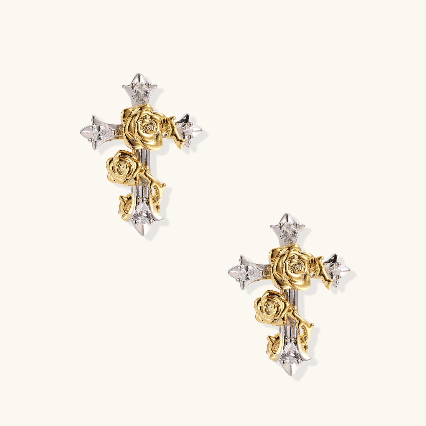 Two-tone cross earrings with gold roses and silver base featuring crystal accents on beige background.