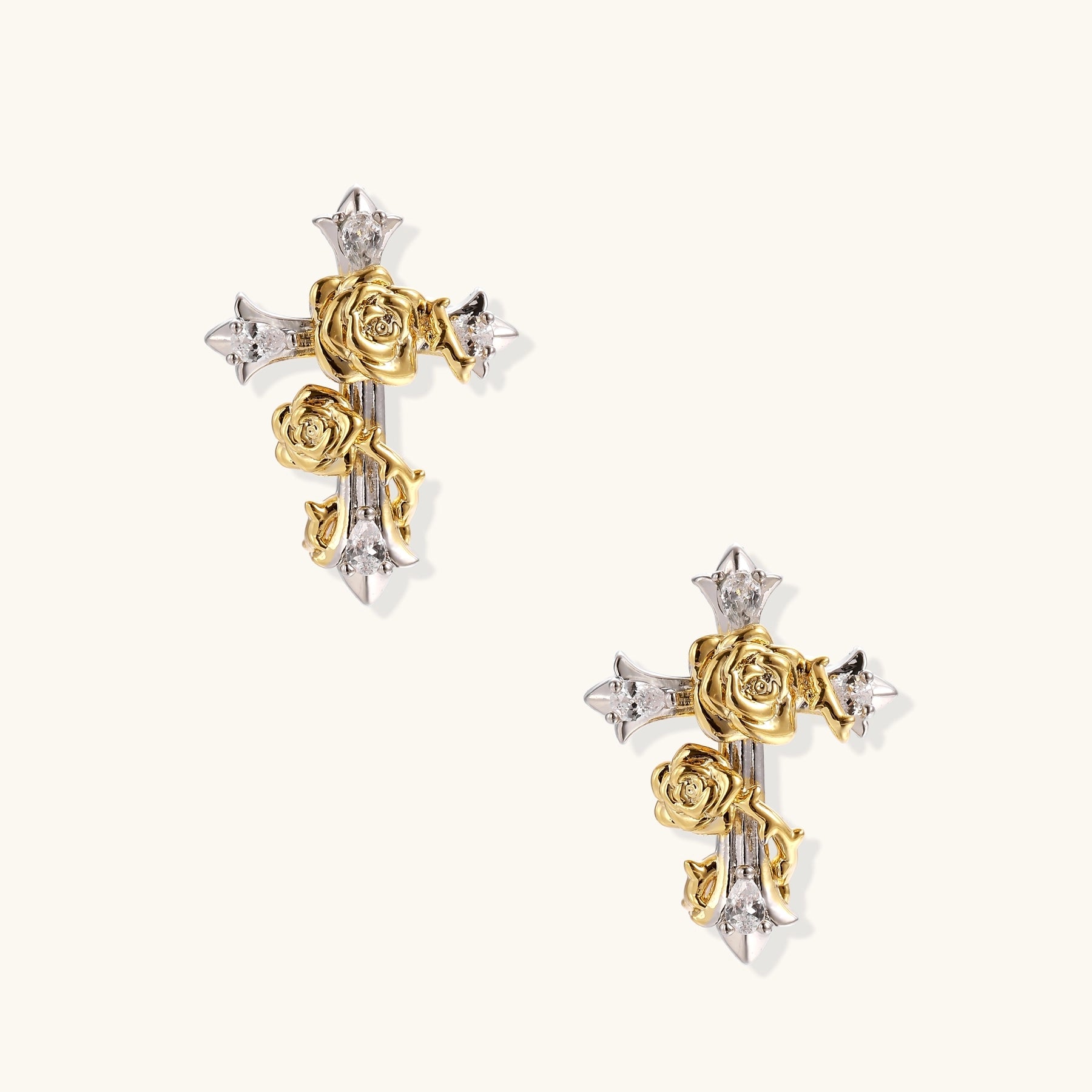 Two-tone cross earrings with gold roses and silver base featuring crystal accents on beige background.