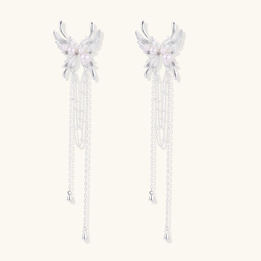 Elegant silver-plated drop earrings with wing-shaped tops, white pearl accents, and long chain tassels on white background.