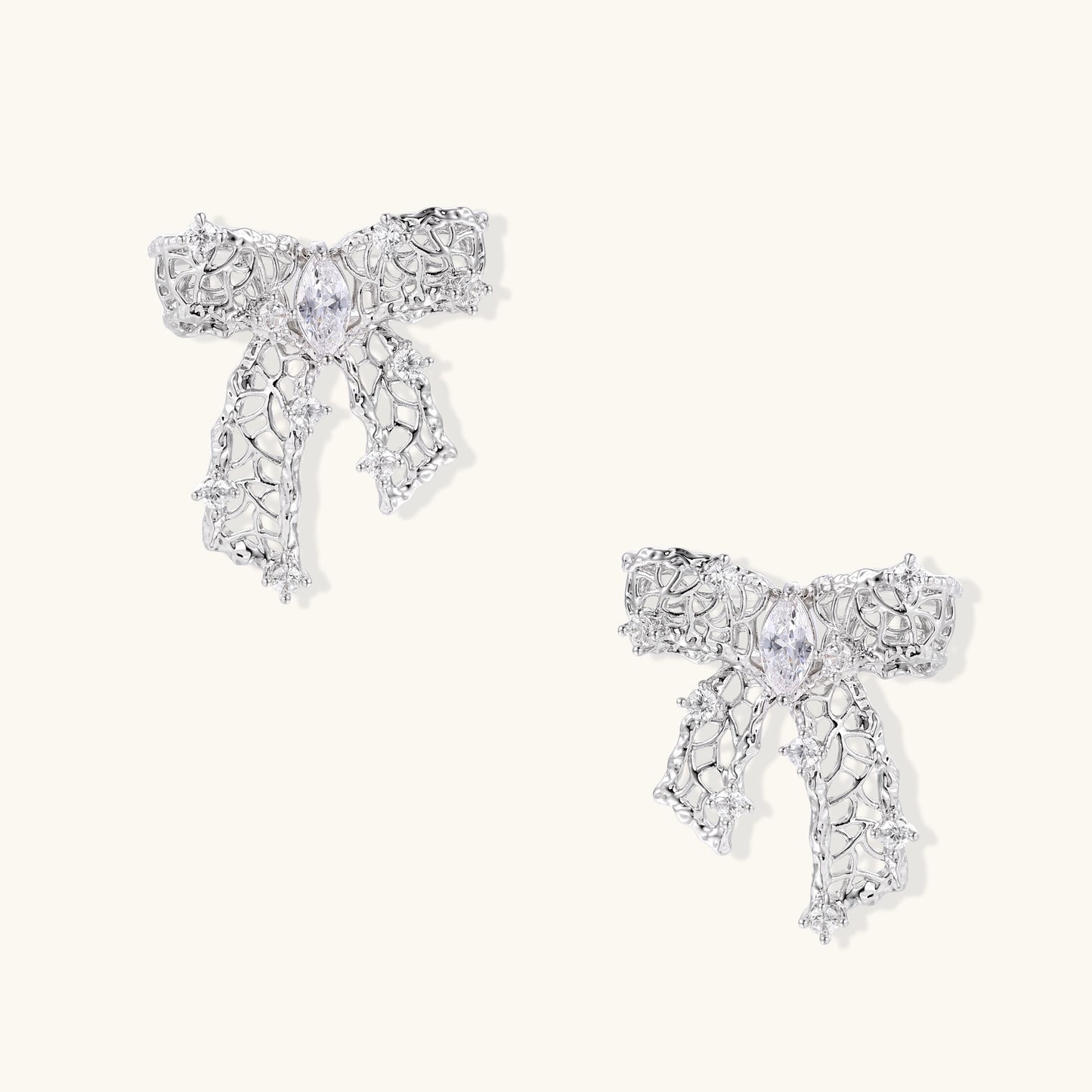 Gold and silver bow-shaped earrings with intricate lattice pattern and clear zirconia stones on neutral background.