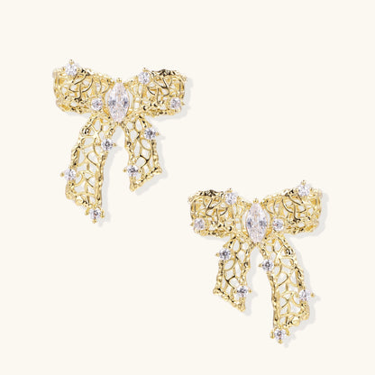 Gold and silver bow-shaped earrings with intricate lattice pattern and clear zirconia stones on neutral background.
