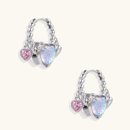 Gold-plated brass hoop earrings with three heart charms including iridescent turquoise and pink hearts on white background.