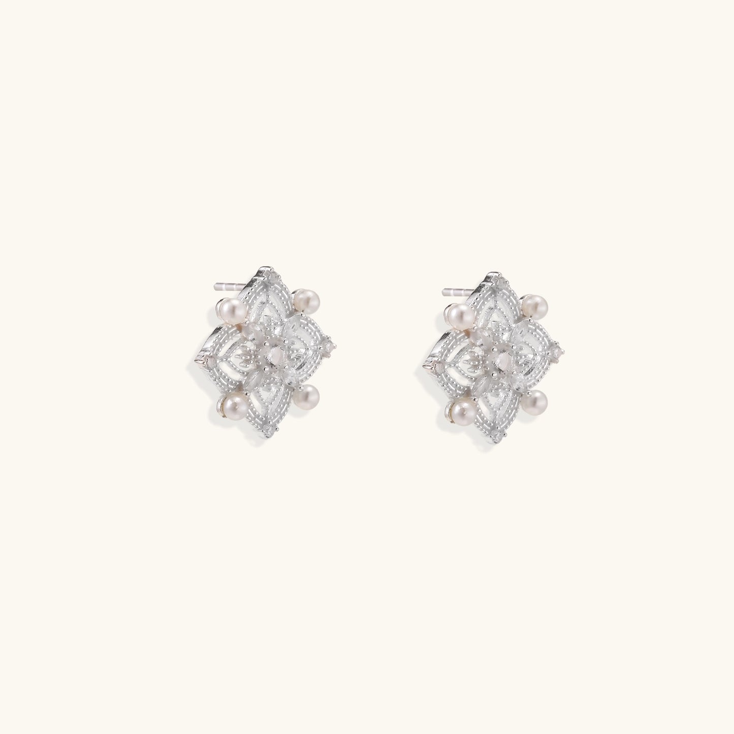 Detailed view of sterling silver stud earrings with geometric filigree design and small freshwater pearls on white background.