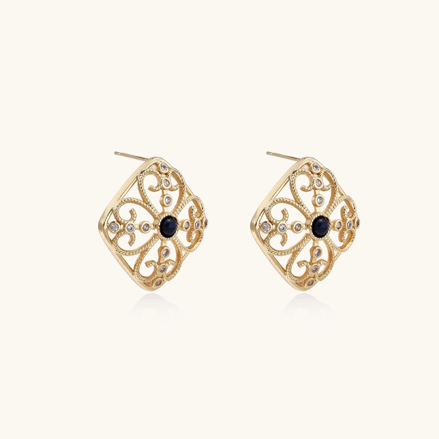 Ornate 18K gold plated stud earrings with intricate filigree design and central lapis lazuli stones on cream background.