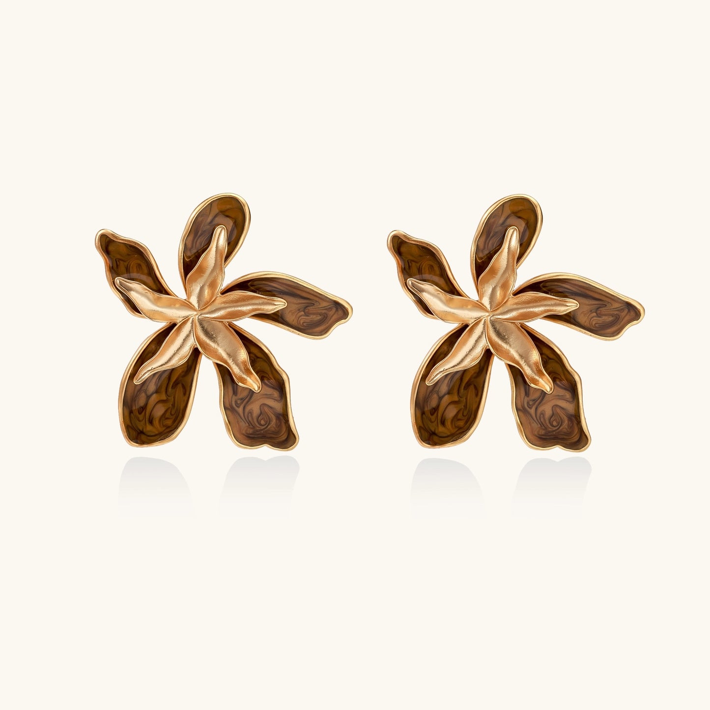 Large gold-plated flower earrings with brown enamel marbled petals on beige background, showing intricate floral design.