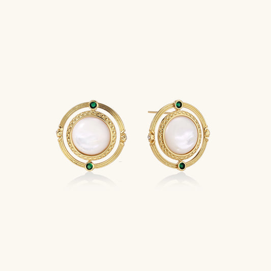 Close-up of gold-plated circular earrings with white mother-of-pearl centers and green zirconia accents on cream background.