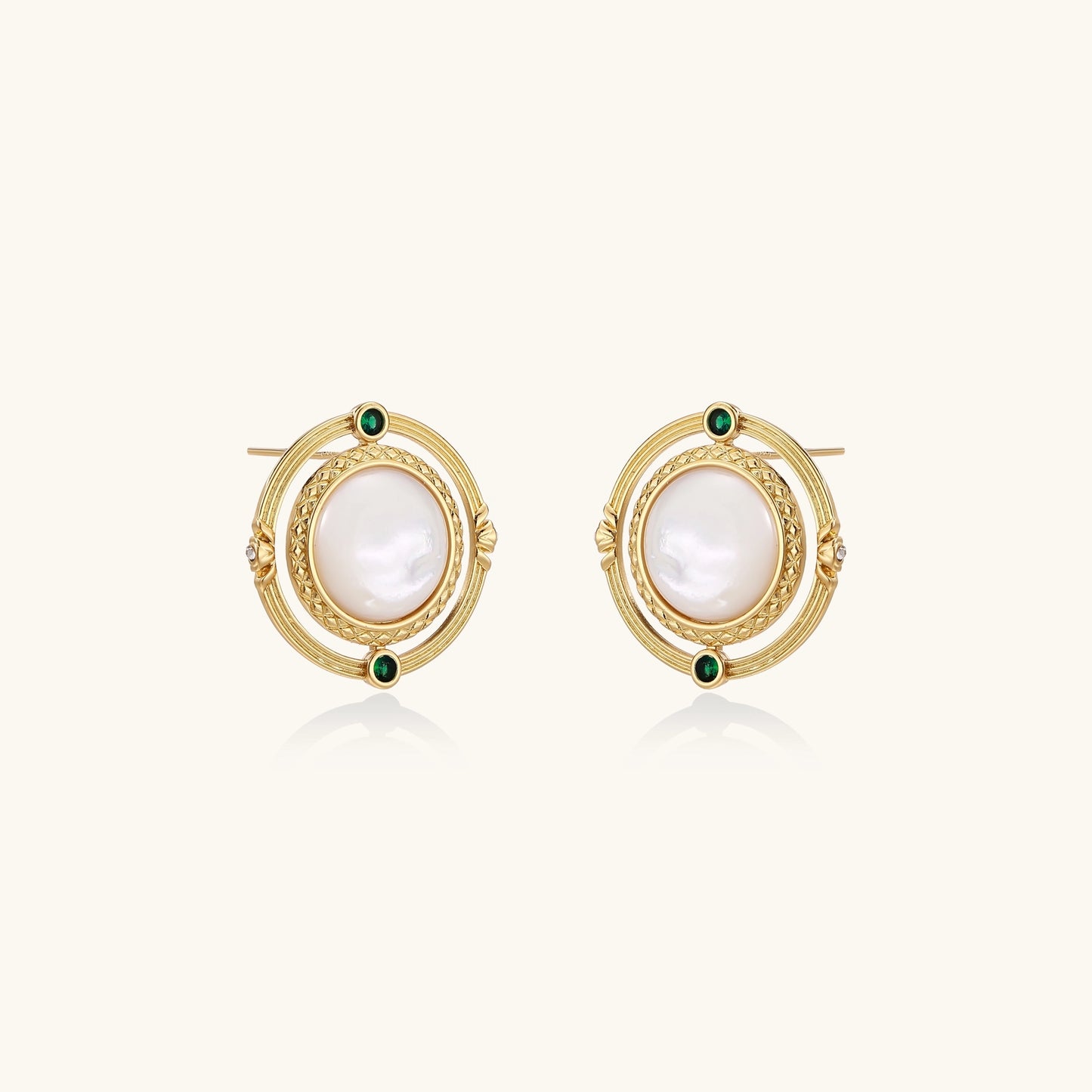 Close-up of gold-plated circular earrings with white mother-of-pearl centers and green zirconia accents on cream background.