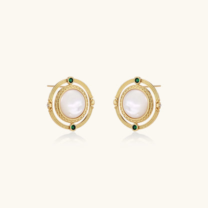 Close-up of gold-plated circular earrings with white mother-of-pearl centers and green zirconia accents on cream background.