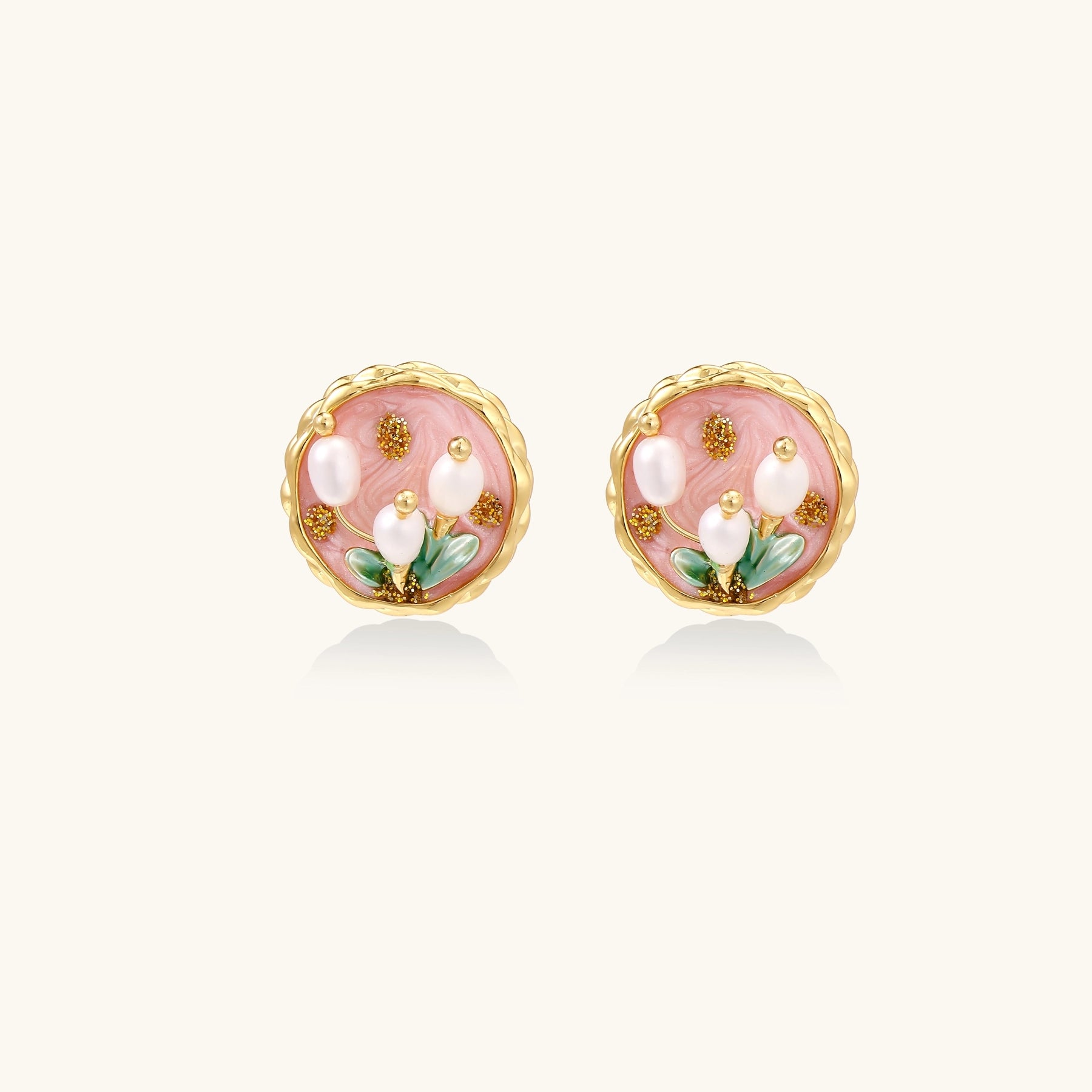 Round stud earrings with pink enamel background, white pearl tulips, green leaves, and twisted gold border on white background.