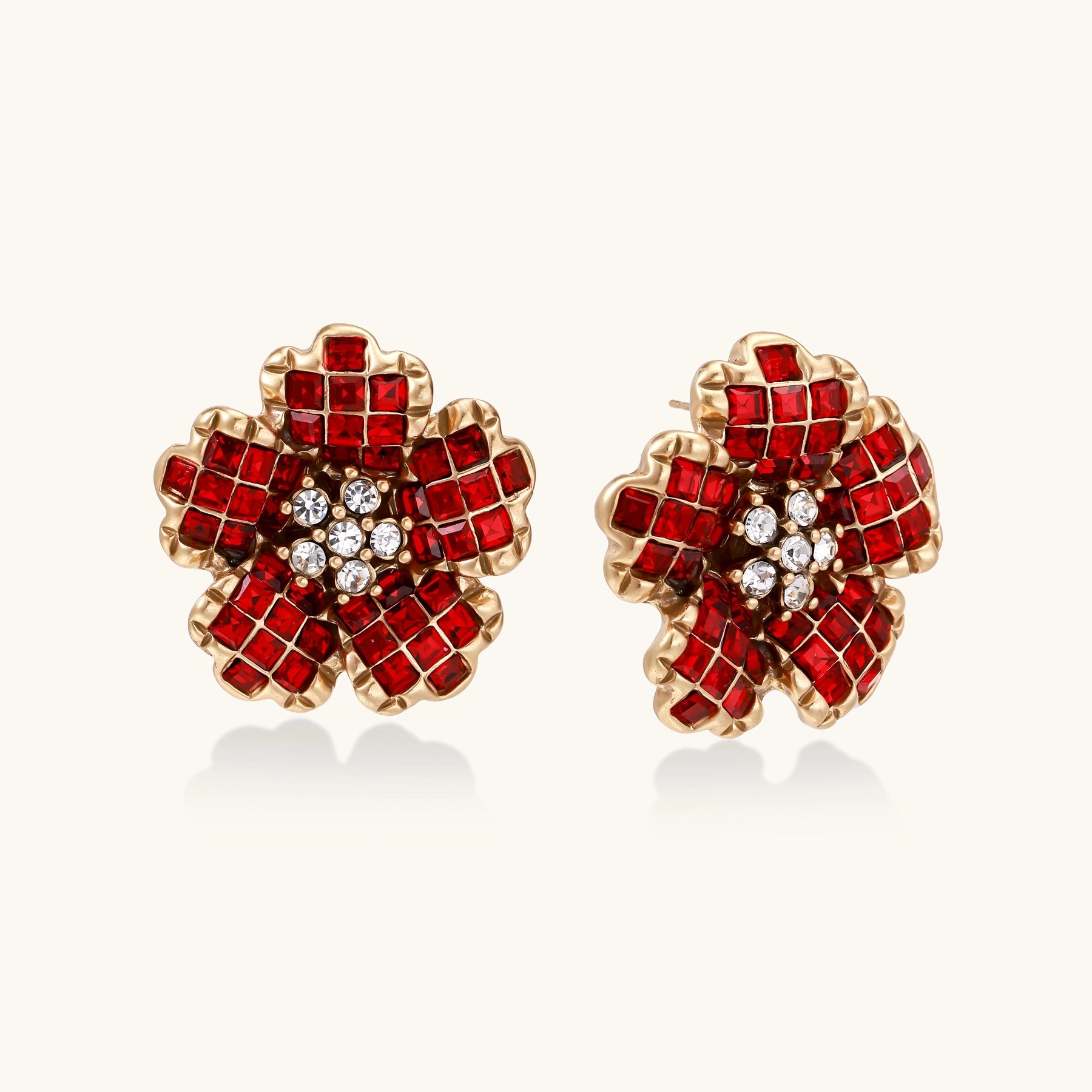 Gold-plated floral stud earrings with layered red crystal petals and clear zirconia centers on cream background.