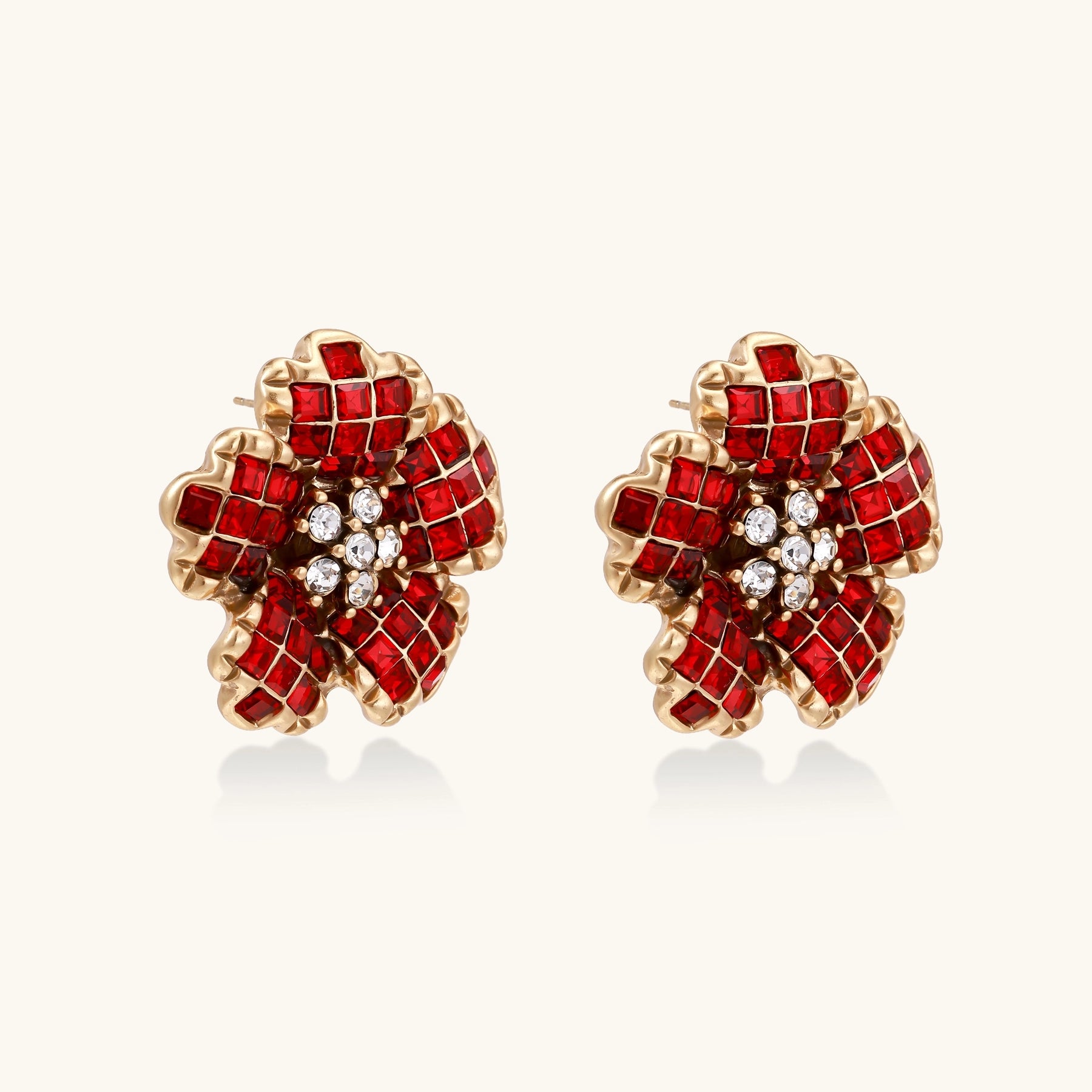 Gold-plated floral stud earrings with layered red crystal petals and clear zirconia centers on cream background.