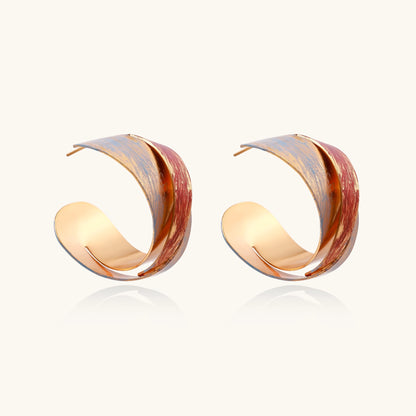 Twisted gold-plated brass earrings with multicolored enamel brushstroke patterns in burgundy and blue on white background.