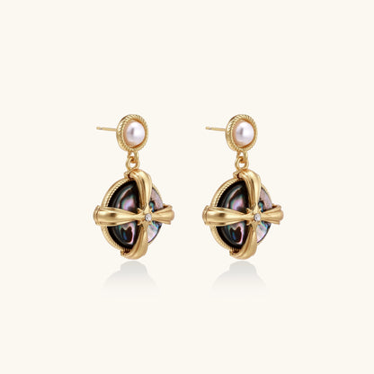 Gold-plated drop earrings with cross design framing iridescent abalone shell and pearl studs on neutral background.