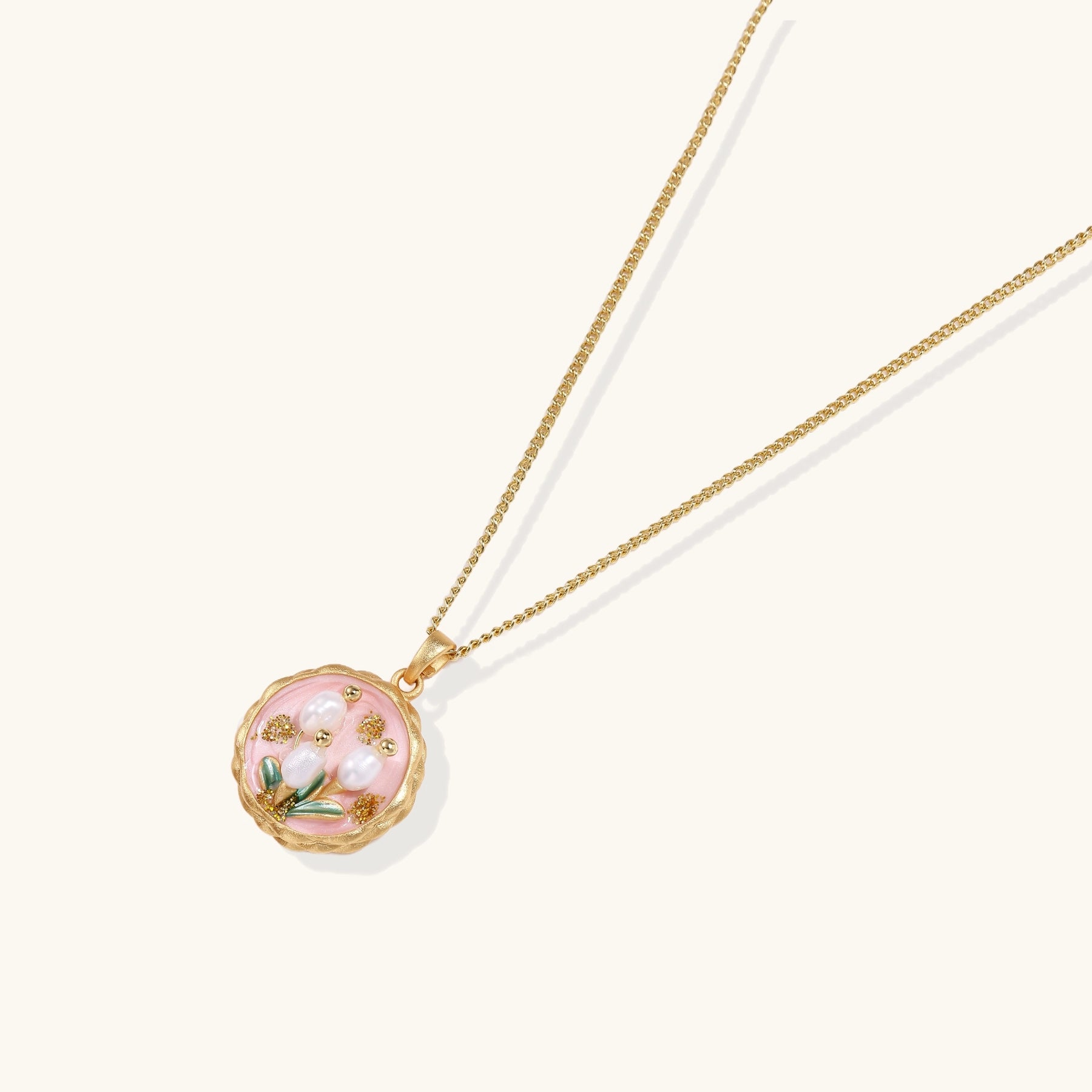 Gold-plated pendant necklace with pink enamel background and white freshwater pearl floral design on neutral background.