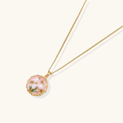 Gold-plated pendant necklace with pink enamel background and white freshwater pearl floral design on neutral background.