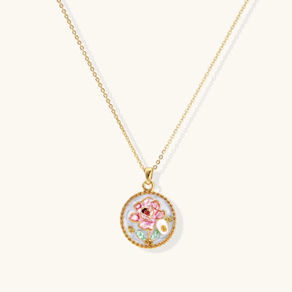Gold-plated circular pendant featuring pink enamel rose with pearl accents and green leaf details on adjustable chain.