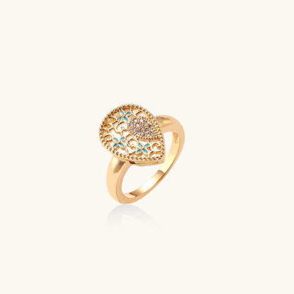 Gold-plated heart ring with turquoise enamel scrollwork and cubic zirconia stones on white background