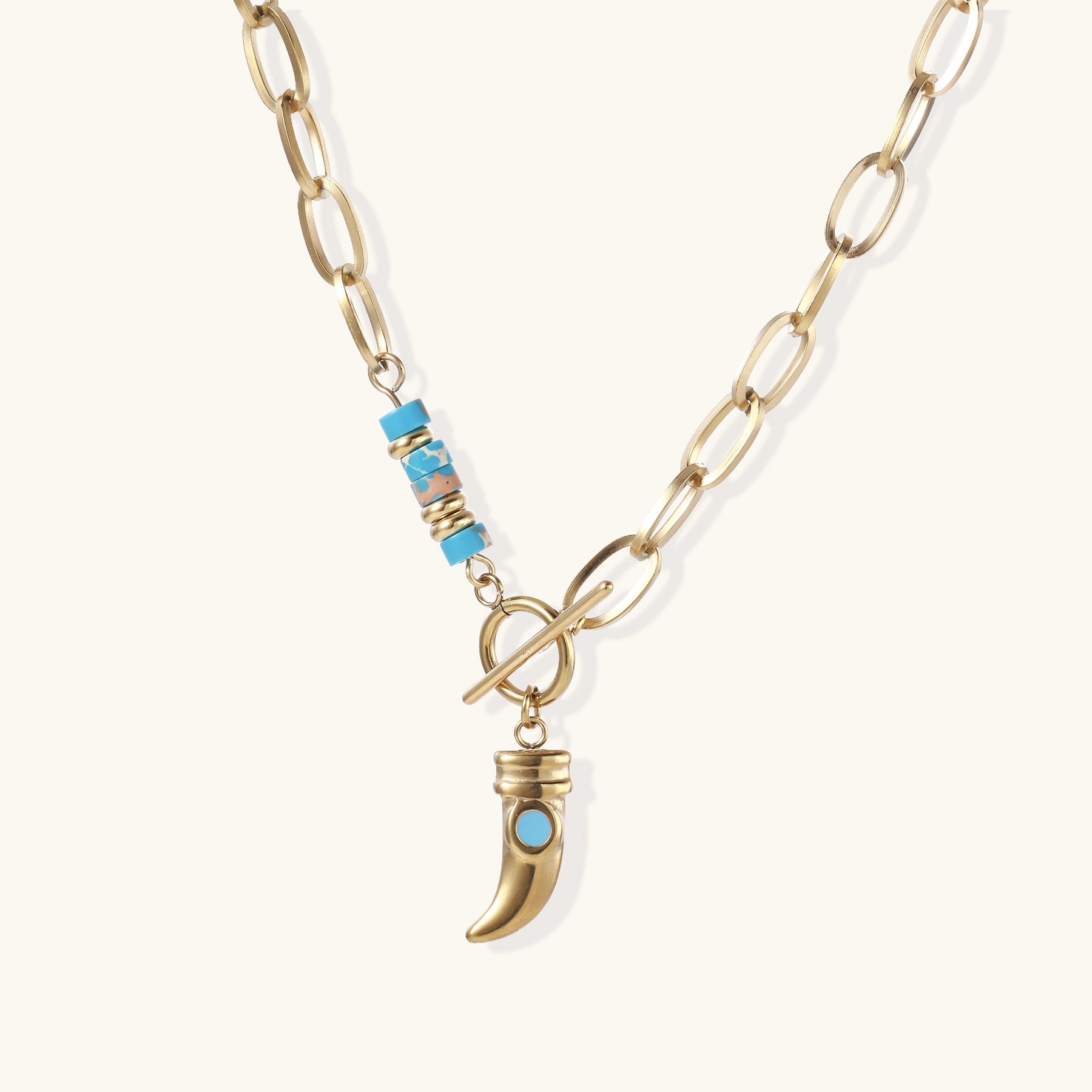 Gold-plated chain necklace with toggle clasp, turquoise beads, and curved horn pendant with inset turquoise stone on light background.