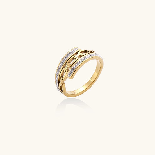 Gold-plated chain-link ring with rhinestone rows on cream background, showing bold geometric design and sparkling details.