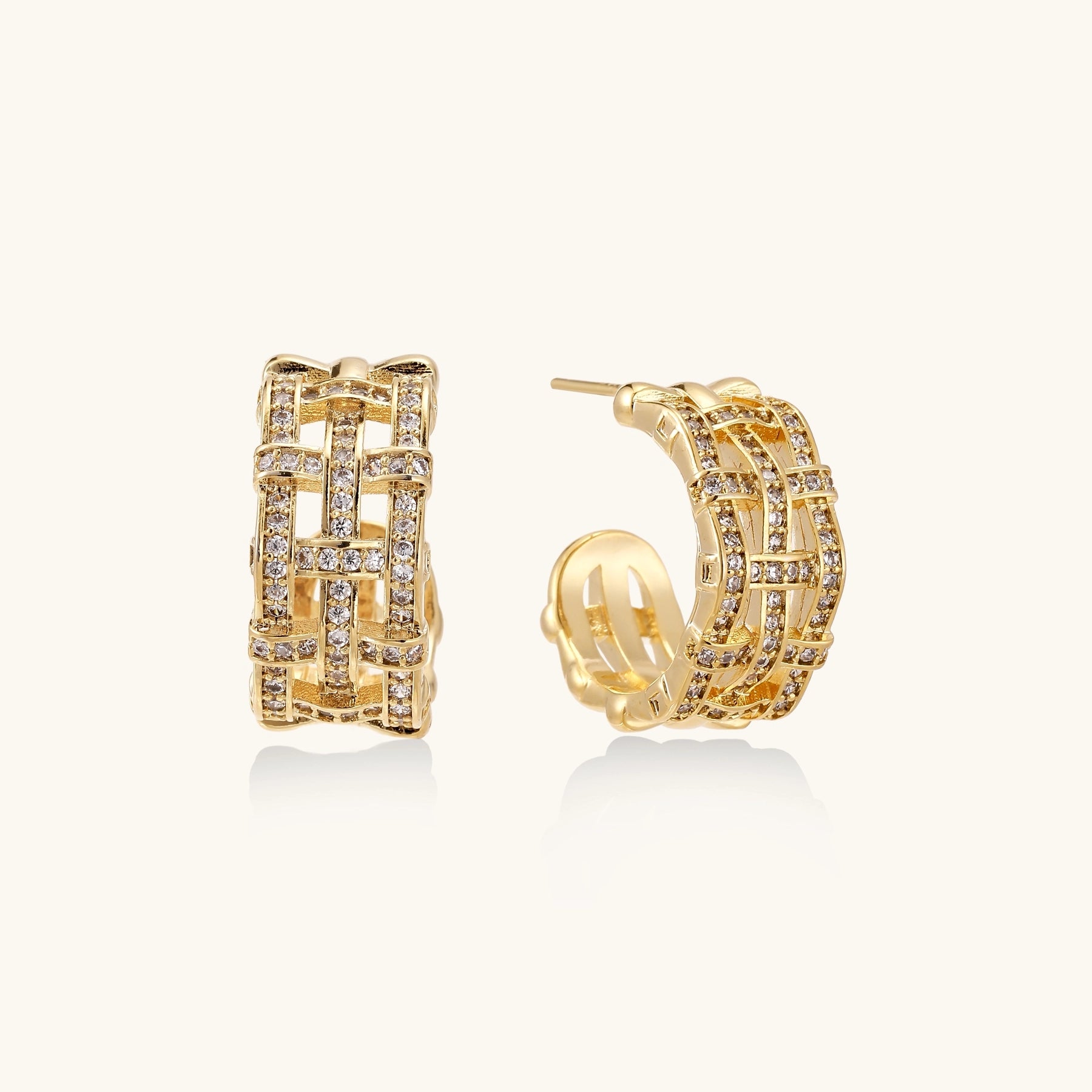 Close-up of geometric gold-plated hoop earrings with crystal pave in intricate lattice pattern on neutral background.