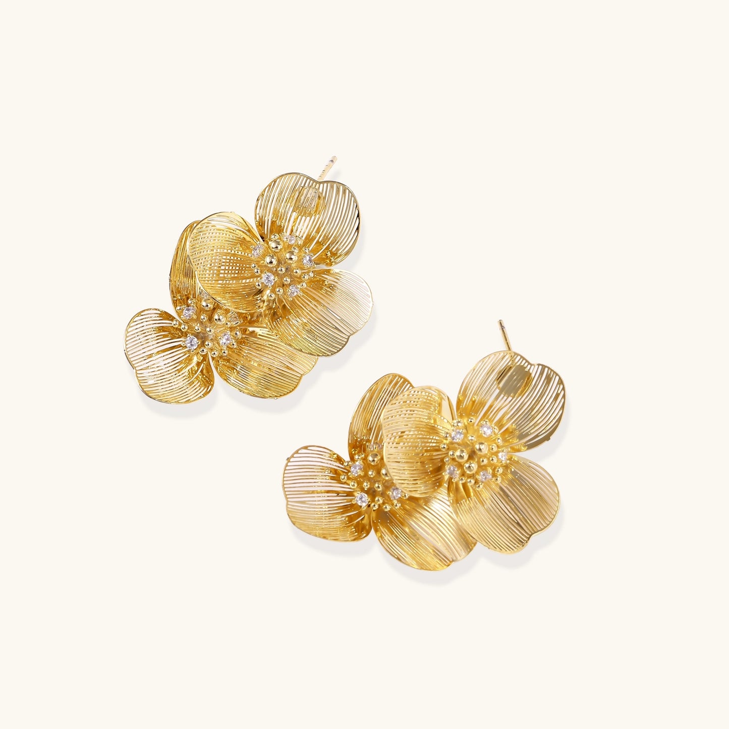 Layered gold-plated floral stud earrings with textured petals and crystal-accented centers on white background.