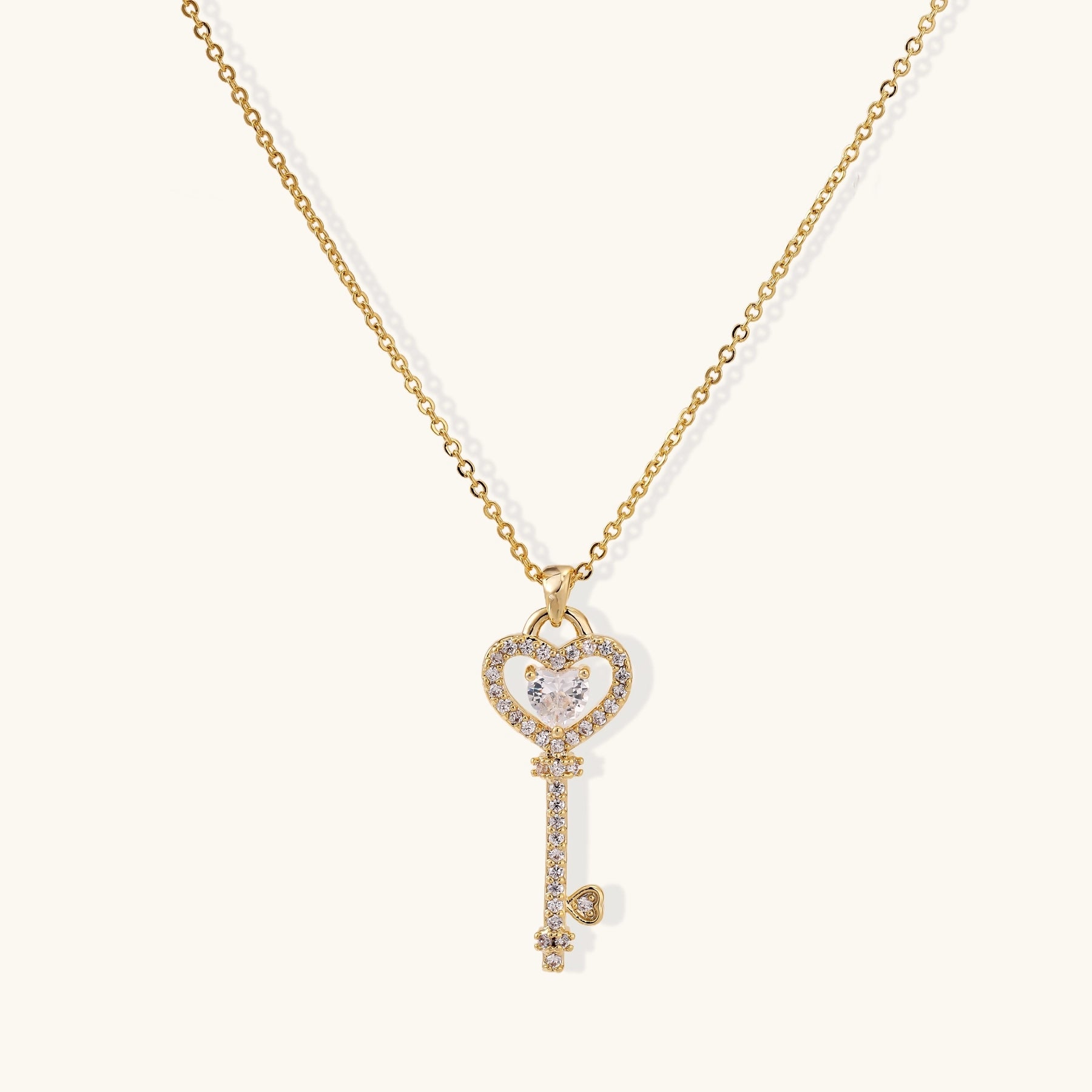 Gold-plated key pendant necklace with heart top and crystal embellishments on adjustable chain against cream background