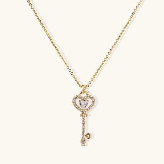 Gold-plated key pendant necklace with heart top and crystal embellishments on adjustable chain against cream background