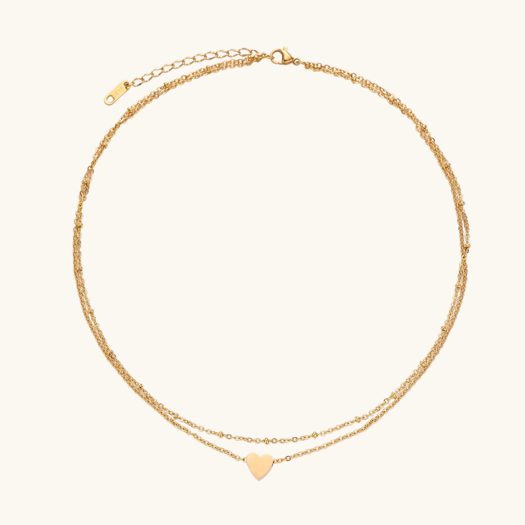 Two-layer gold-plated stainless steel necklace with small heart pendant displayed on beige background