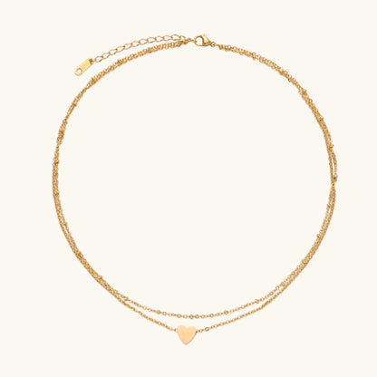 Two-layer gold-plated stainless steel necklace with small heart pendant displayed on beige background