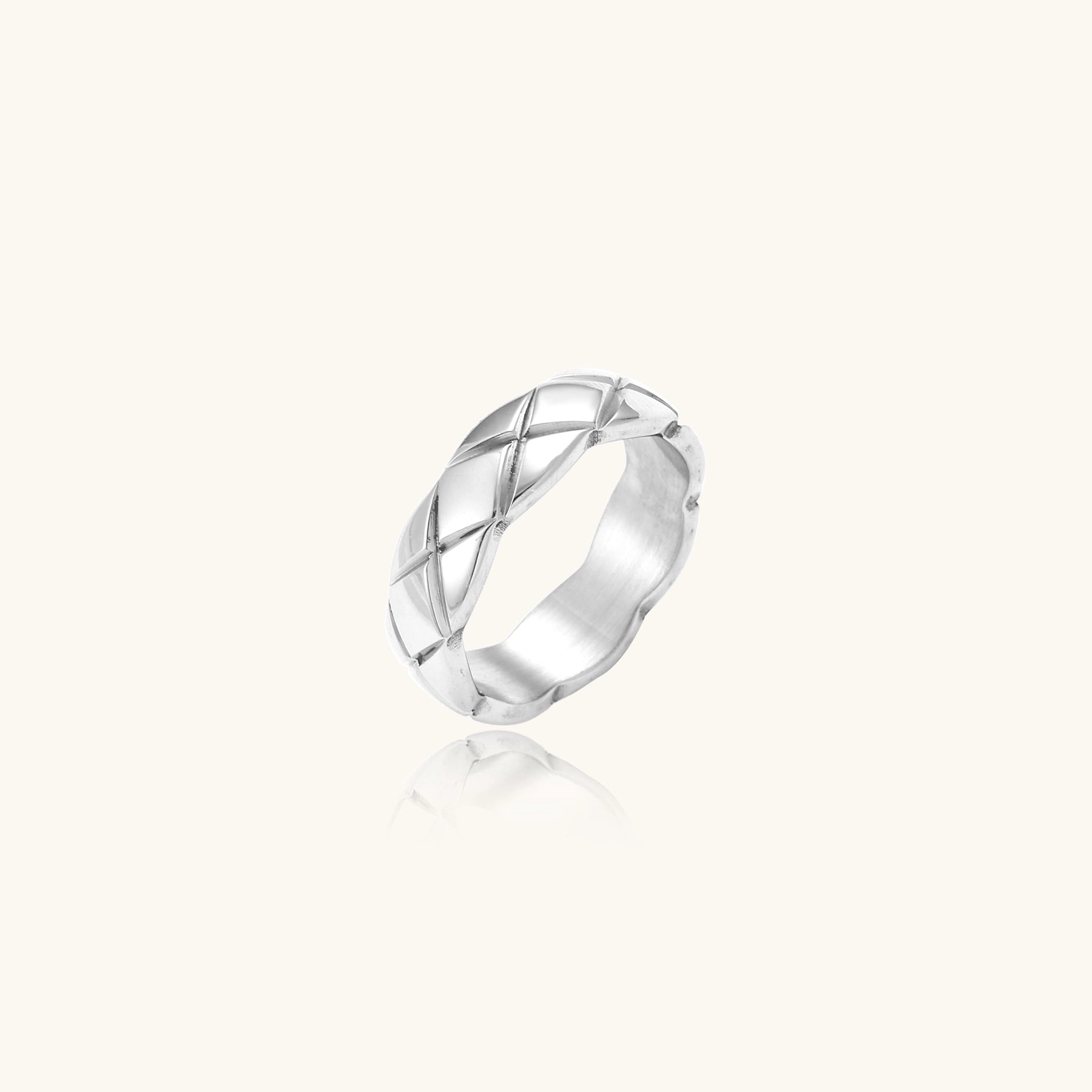 Close-up of a polished stainless steel ring featuring a geometric quilted diamond pattern on white background.