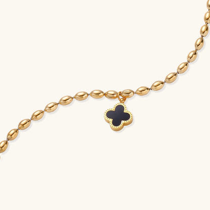 Dainty gold-plated beaded bracelet with oval links and four-leaf clover charm pendant on neutral background.