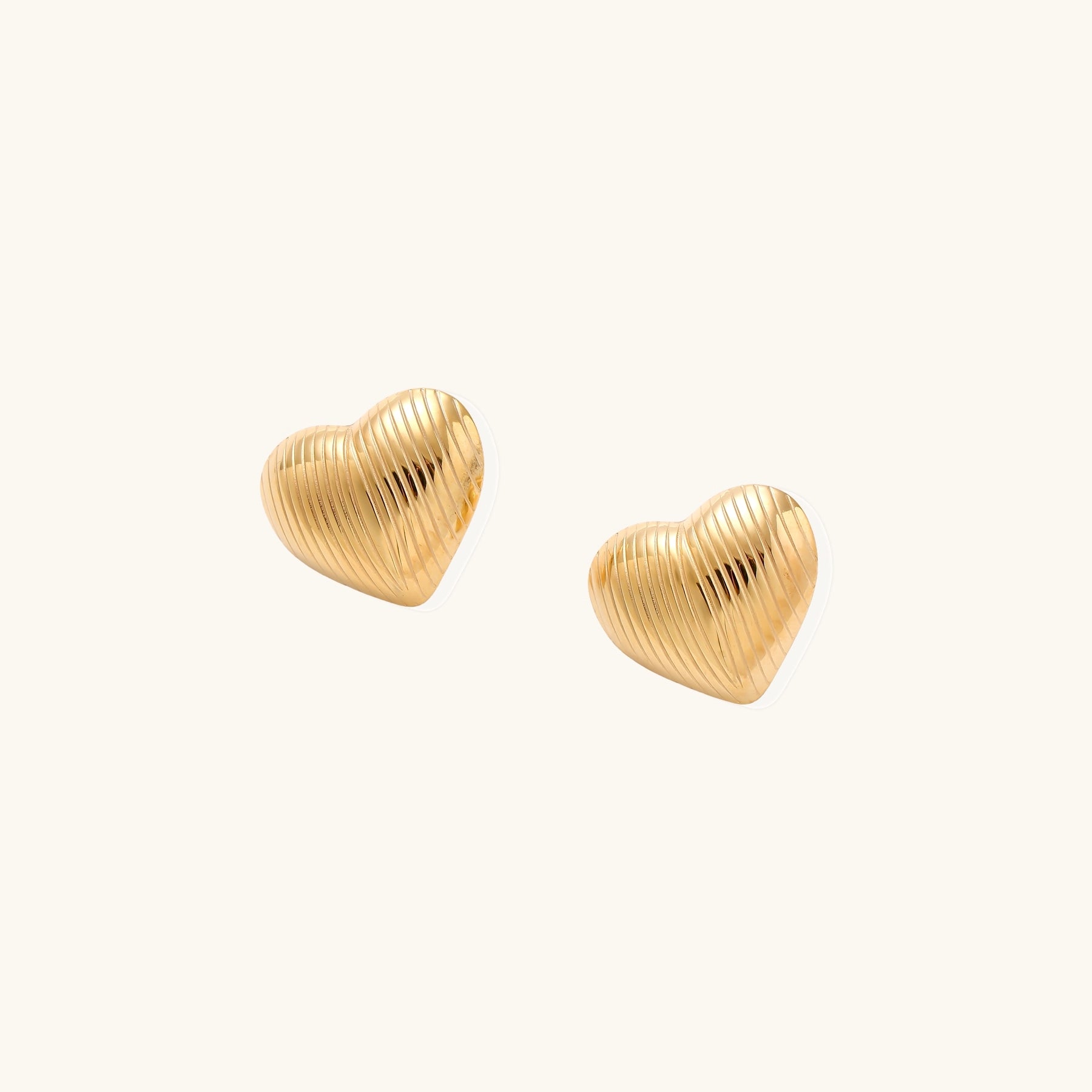 Close-up of ridged heart-shaped gold-plated stud earrings with textured surface pattern on cream background.
