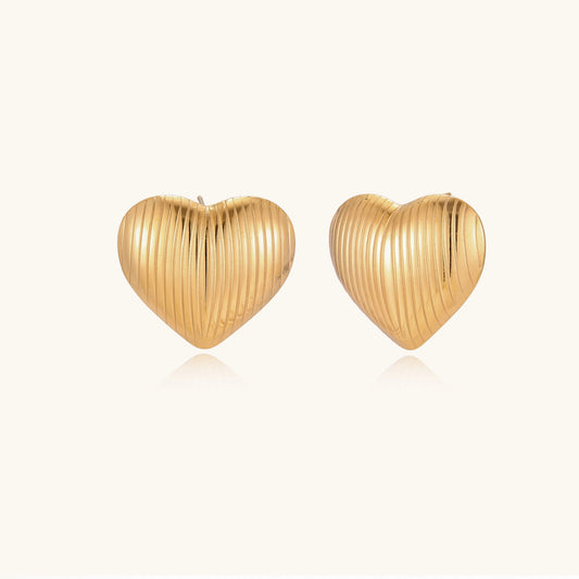 Close-up of ridged heart-shaped gold-plated stud earrings with textured surface pattern on cream background.