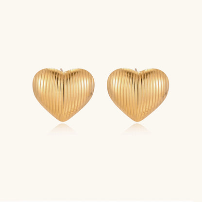 Close-up of ridged heart-shaped gold-plated stud earrings with textured surface pattern on cream background.