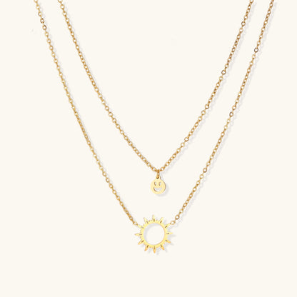 Delicate gold-plated layered necklace with smiley face and sun pendants on white background, showing adjustable chain.